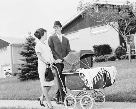a man and woman pushing a crib in a suburban neighborhood